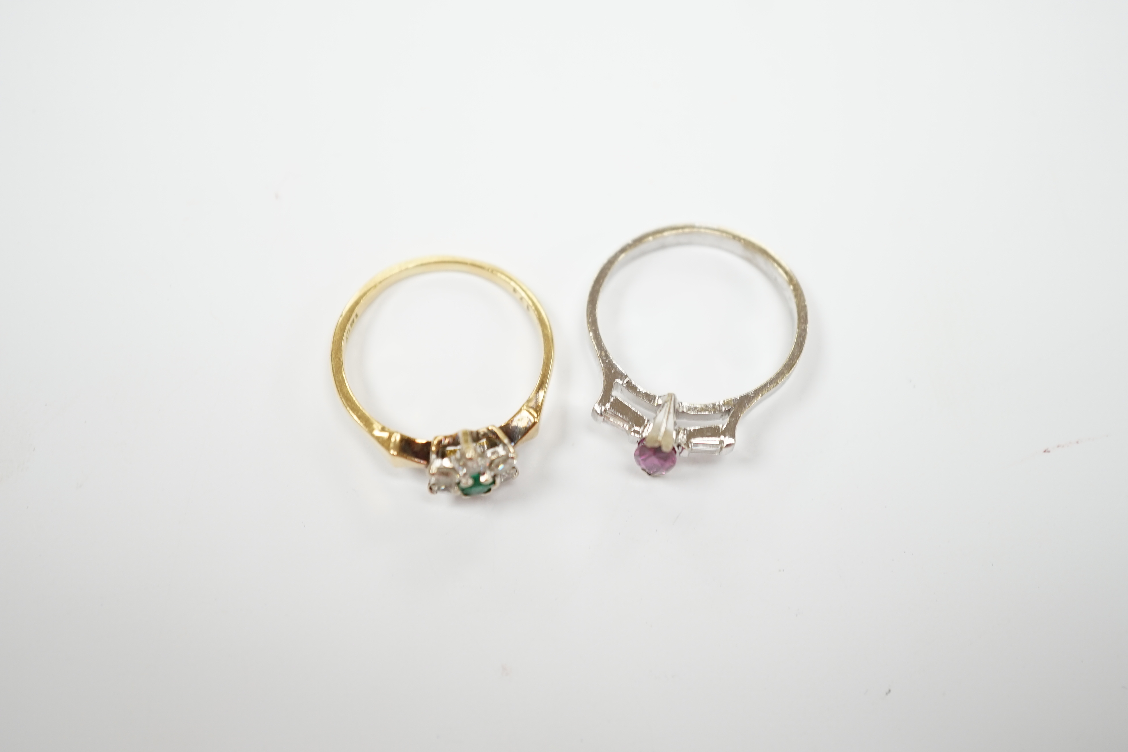 An 18ct, emerald and diamond set flower head cluster ring, size N and an 18ct white metal ruby and diamond set three stone ring, size L/M, gross weight 6.2 grams.